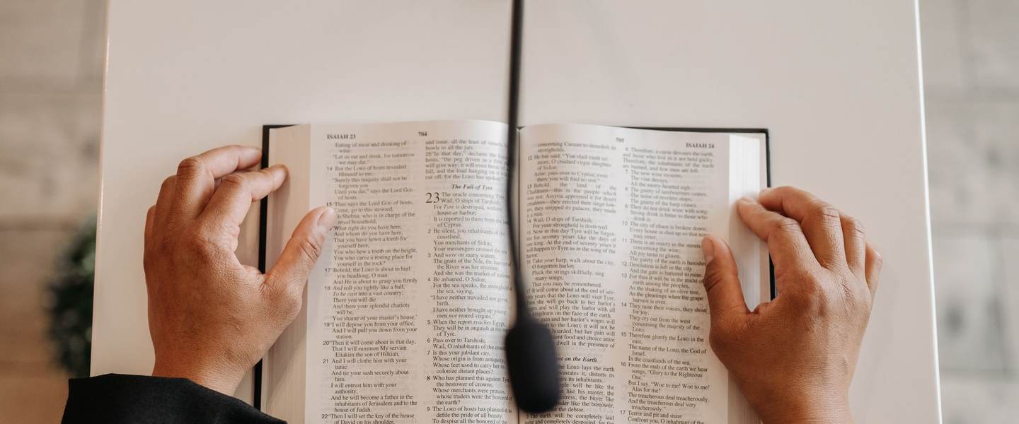 Hands resting on an open Bible at a podium with a microphone
