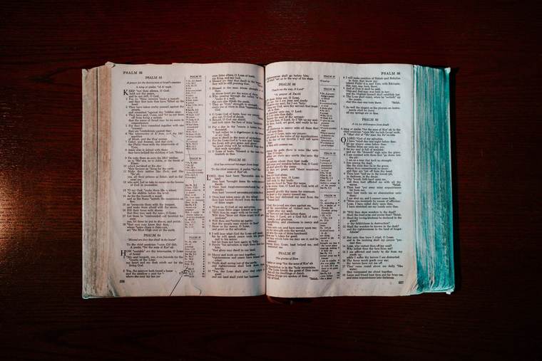 An open Bible on a dark wooden table, seen from above