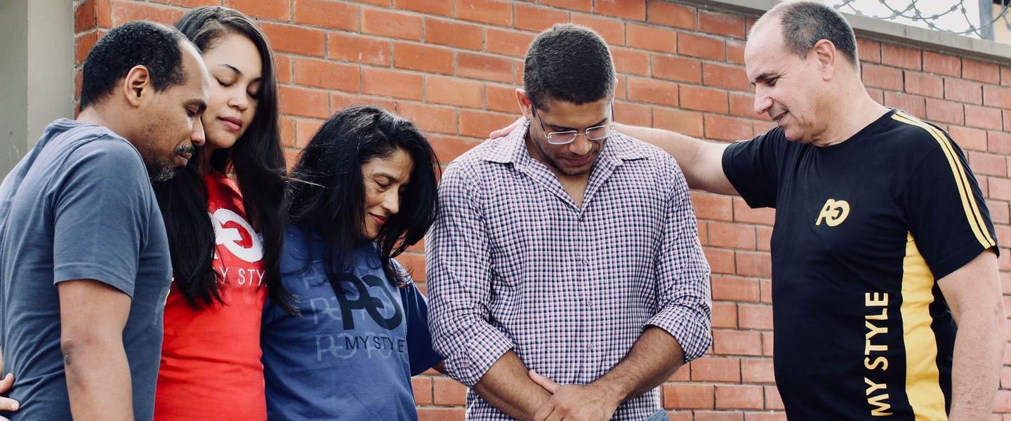 A small group of adults praying together with bowed heads