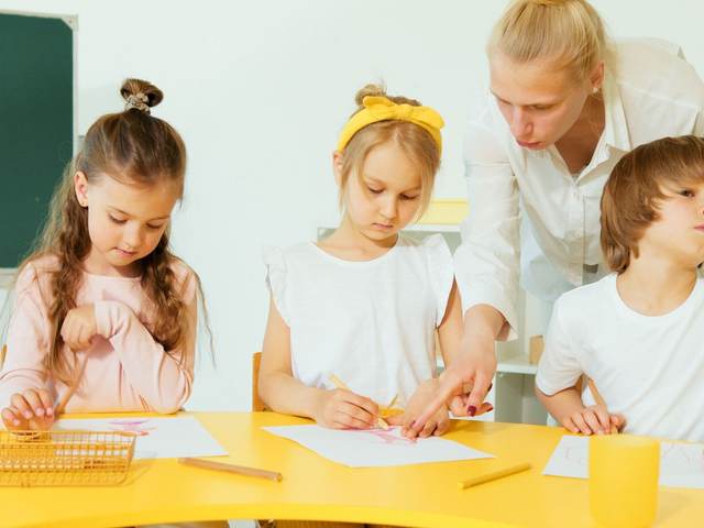 A teacher helping young children draw at a classroom table