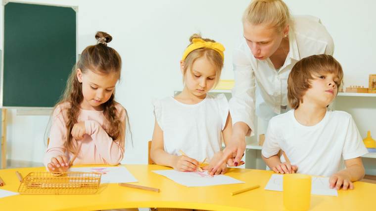 A teacher helping young children draw at a classroom table