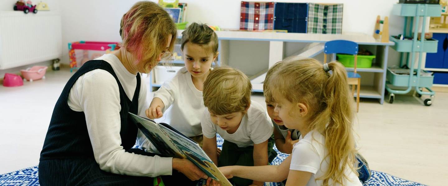 A teacher reading a picture book to preschoolers sitting on a rug