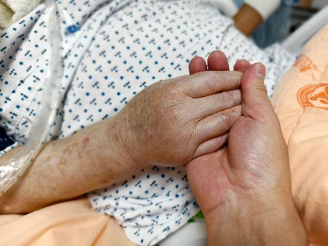 A hand holding the hand of a patient in a hospital bed