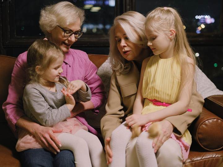 A grandmother, a mother, and two young girls sitting close together on a sofa