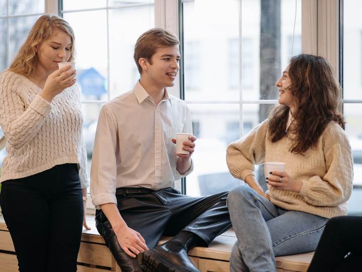 Three young adults laughing and talking over coffee by a window