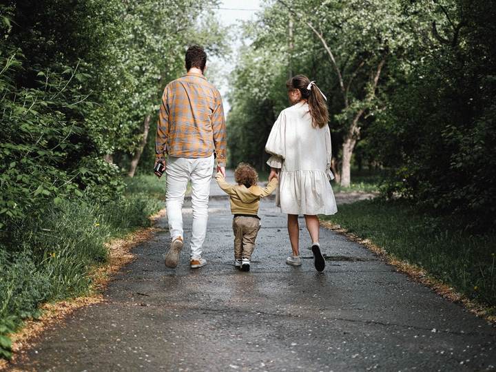 A young family walking hand in hand with their toddler on a tree-lined path